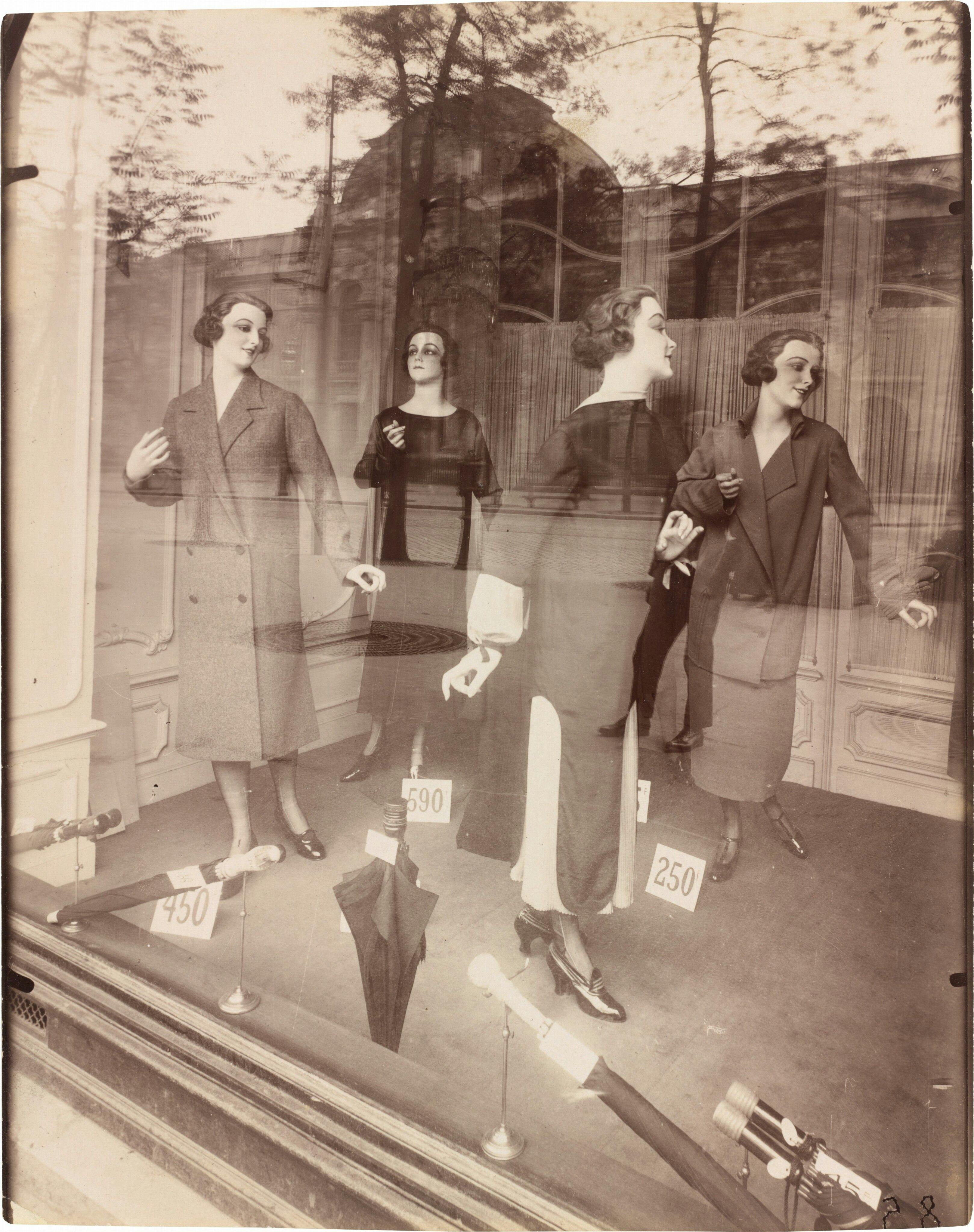 sepia photograph of a women's fashion storefront, female mannequins in dresses with price tags, reflective glass with tree silhouette, by Eugène Atget